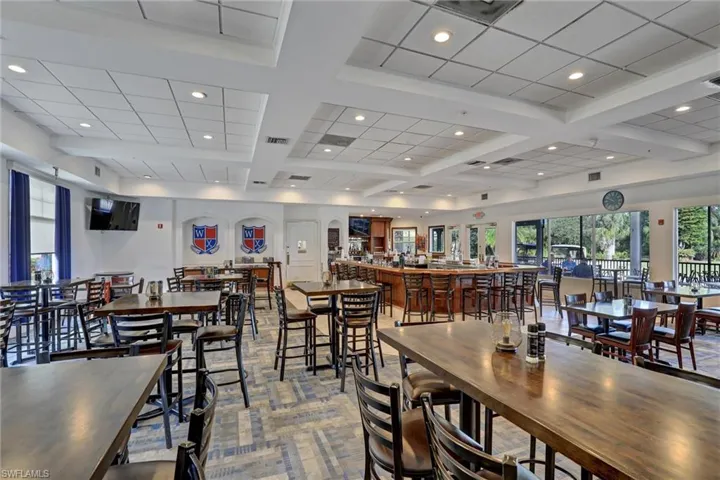 Spacious common area featuring a full-service bar with wood paneling, ample seating, recessed lighting, and a suspended ceiling system