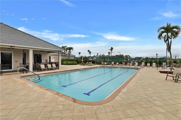 Outdoor swimming pool with integrated lane lines, surrounded by a light-toned paver deck, and an adjacent structure with a tiled roof