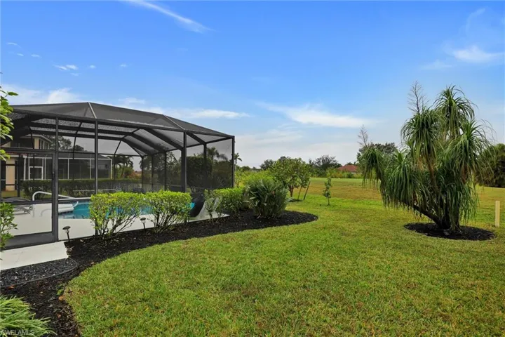 Screened pool enclosure featuring a concrete deck and lush perimeter landscaping