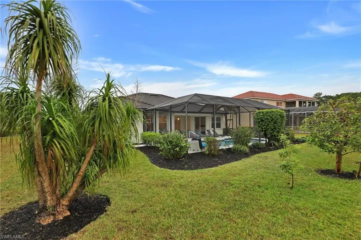 Spacious backyard featuring a screened pool enclosure, mature tropical landscaping, and a manicured lawn