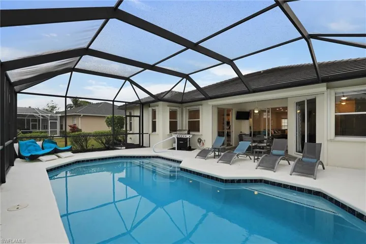 Screened swimming pool enclosure featuring a hexagonal pool with a blue tile border, a spacious deck, and direct access to interior spaces via sliding glass doors