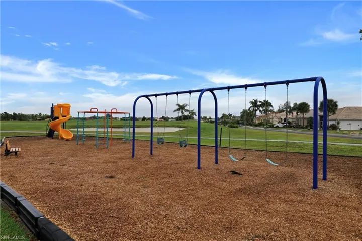 Community playground with a swing set, slide, and monkey bars over wood chip surfacing