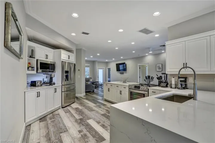 Open concept kitchen featuring white cabinetry, quartz countertops, stainless steel appliances, recessed lighting, and wood-finish flooring