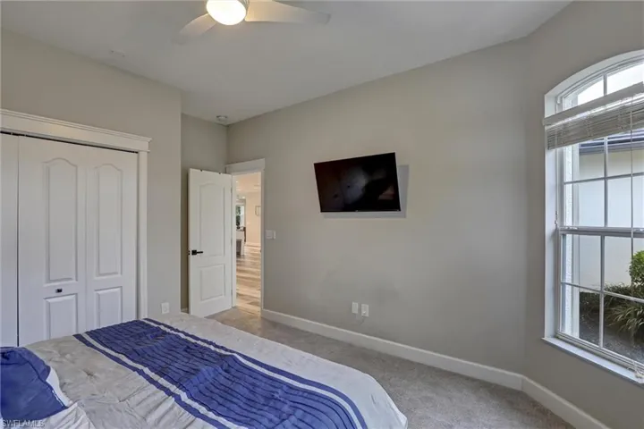 Carpeted room featuring a ceiling fan, arched window with horizontal blinds, bi-fold closet doors, and light gray wall paint