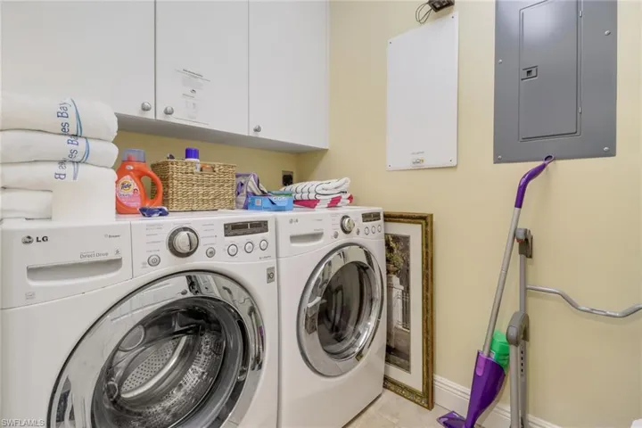 Laundry room featuring light tile patterned floors, cabinets, electric panel, and washing machine and clothes dryer
