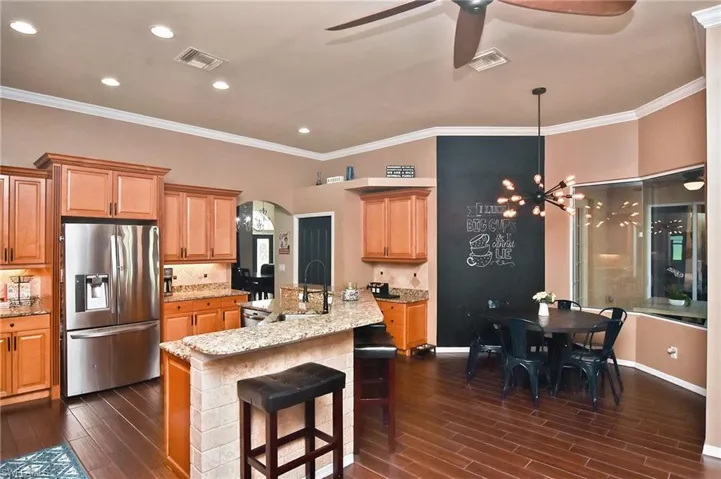Kitchen with stainless steel refrigerator with ice dispenser, a kitchen island with sink, crown molding, light stone counters, and decorative backsplash
