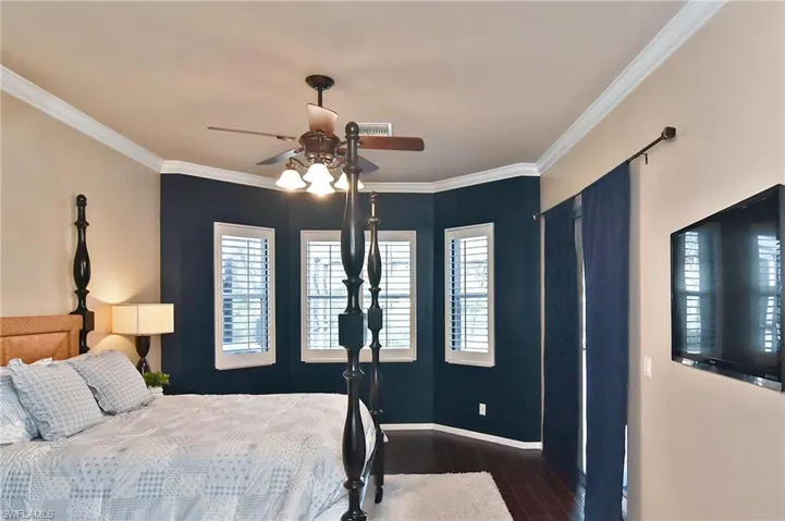 Bedroom with ornamental molding, dark wood-style floors, and a ceiling fan