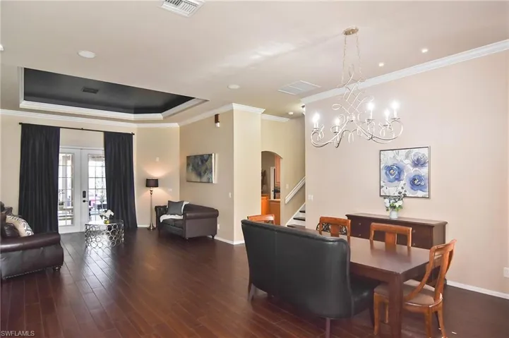 Dining room featuring ornamental molding, a tray ceiling, arched walkways, dark wood finished floors, and french doors
