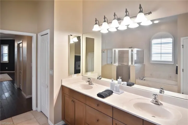 Bathroom featuring double vanity, a garden tub, a stall shower, and light tile patterned floors
