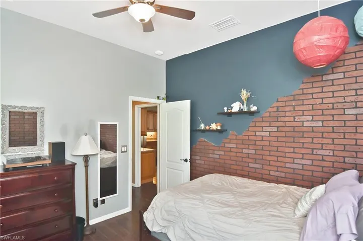 Bedroom featuring dark wood-style flooring, brick wall, an accent wall, and a ceiling fan