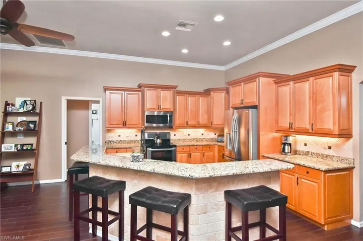 Kitchen with tasteful backsplash, stainless steel appliances, light stone countertops, ornamental molding, and a breakfast bar
