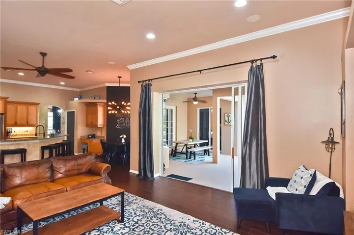 Living room featuring a ceiling fan, dark wood-type flooring, crown molding, a chandelier, and arched walkways