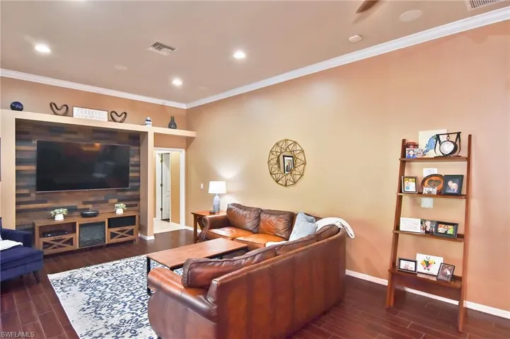Living room with wood finish floors, ornamental molding, and recessed lighting