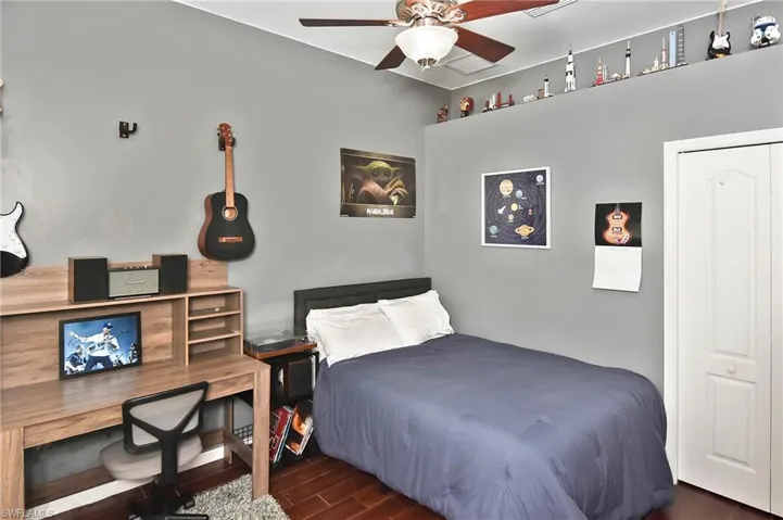 Bedroom with wood finish floors, a desk, a ceiling fan, and a closet