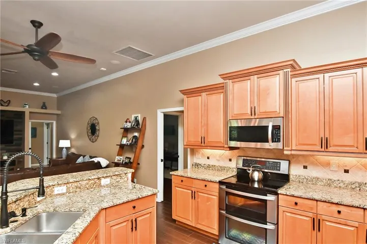 Kitchen with stainless steel appliances, open floor plan, light stone counters, ornamental molding, and wood tiled floors