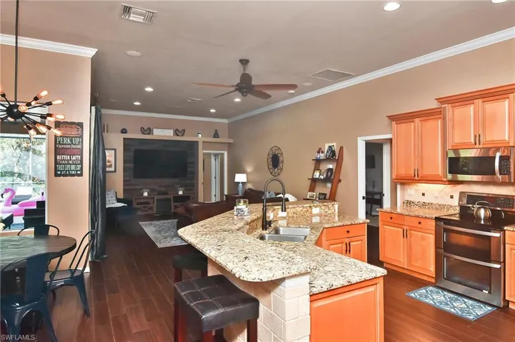 Kitchen featuring stainless steel appliances, ceiling fan, light stone countertops, crown molding, and dark wood finished floors