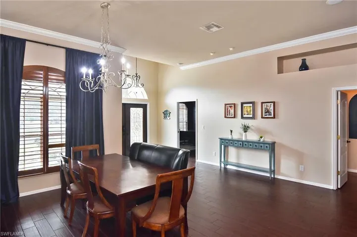 Dining space with dark wood-type flooring, crown molding, and suspended lighting
