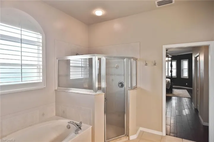 Bathroom featuring connected bathroom, a stall shower, a garden tub, and a ceiling fan