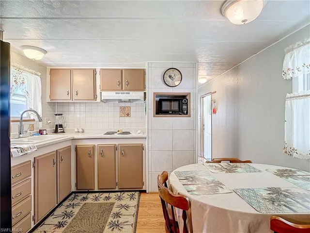 Kitchen with light hardwood / wood-style flooring, white gas stovetop, black microwave, a textured ceiling, and sink