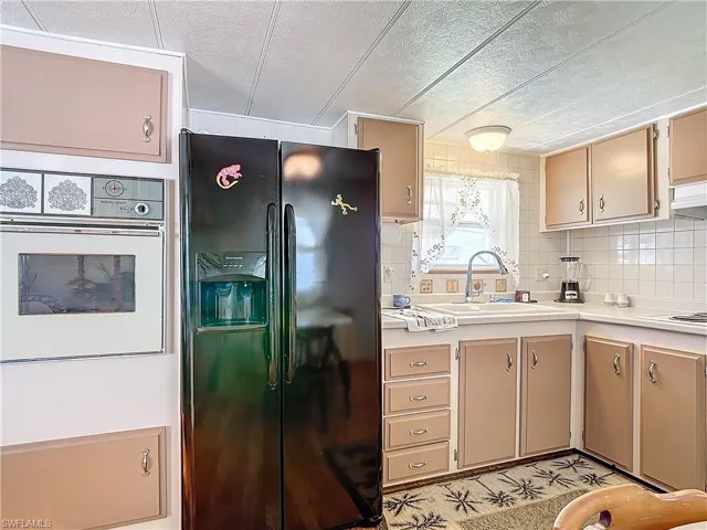 Kitchen featuring black refrigerator with ice dispenser, backsplash, oven, sink, and a textured ceiling