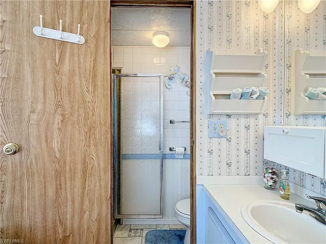 Bathroom with tile flooring, oversized vanity, a textured ceiling, a shower with shower door, and toilet