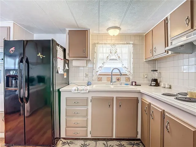 Kitchen with white electric cooktop, black fridge, a textured ceiling, backsplash, and sink