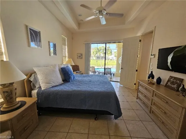 Bedroom featuring light tile patterned flooring, a raised ceiling, access to exterior, and a ceiling fan