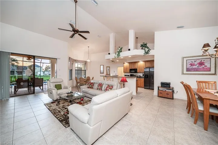 Living room featuring a chandelier, high vaulted ceiling, light tile patterned flooring, and a ceiling fan
