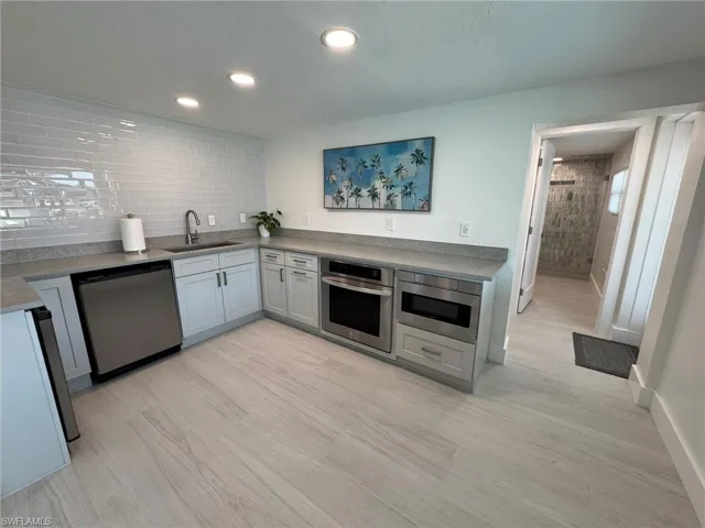 DOWNSTAIRS Kitchen featuring appliances with stainless steel finishes, light hardwood / wood-style floors, sink, and decorative backsplash