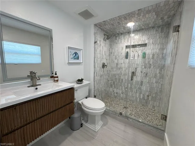 DOWNSTAIRS / POOL Bathroom with vanity, a shower with shower door, and toilet