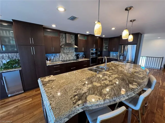 Kitchen with pendant lighting, sink, dark brown cabinetry, stainless steel appliances, and wall chimney range hood