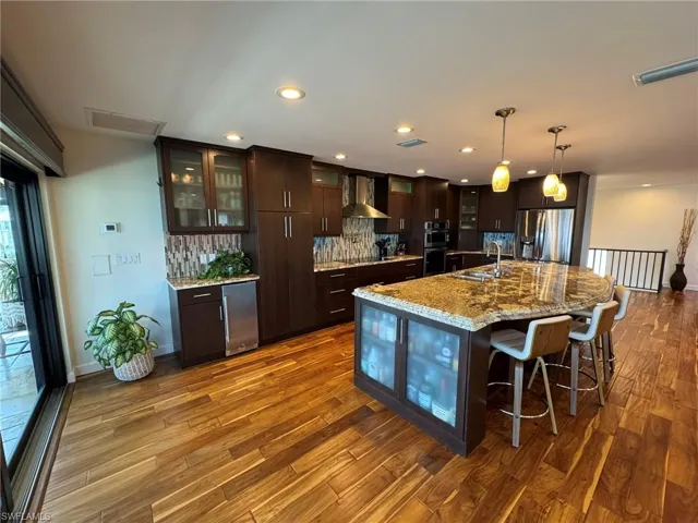 Kitchen with sink, hanging light fixtures, dark brown cabinets, appliances with stainless steel finishes, and wall chimney range hood