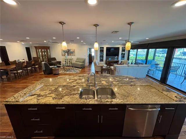 Kitchen featuring sink, a kitchen island with sink, stainless steel dishwasher, dark brown cabinetry, and light stone counters