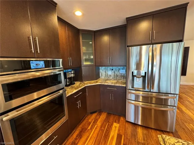 Kitchen featuring stainless steel appliances, dark hardwood / wood-style floors, light stone countertops, and dark brown cabinets
