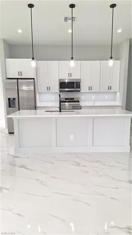 Kitchen featuring stainless steel range with electric stovetop, refrigerator, light marble finish floors, light countertops, and white cabinets
