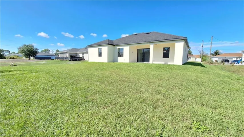 Back of house featuring a yard, stucco siding, a patio, and roof with shingles