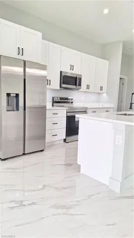 Kitchen with refrigerator, stainless steel range with electric cooktop, a sink, light marble finish floors, and white cabinets