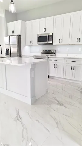 Kitchen featuring built in fridge, stove, light marble finish flooring, and a center island