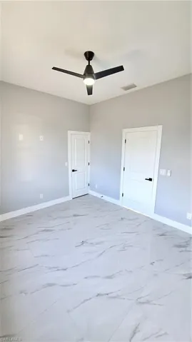 Empty room with baseboards, marble finish floor, visible vents, and a ceiling fan