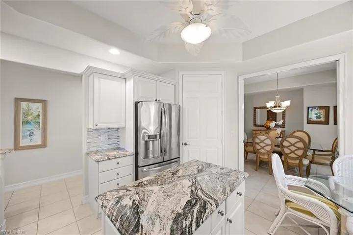 Kitchen with white cabinets, light stone countertops, stainless steel fridge, a chandelier, and recessed lighting