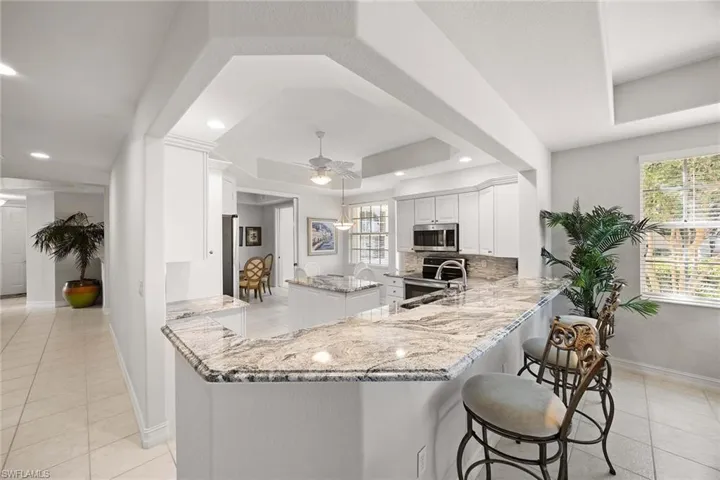 Kitchen with a kitchen island, white cabinets, light stone counters, a raised ceiling, and a peninsula