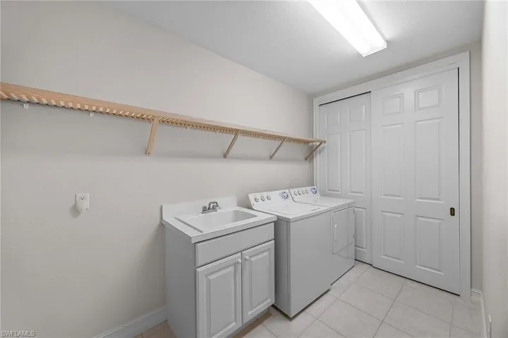 Washroom with light tile patterned flooring, washer and dryer, and cabinet space