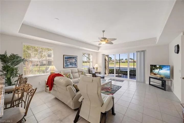 Living room with a raised ceiling, light tile patterned flooring, and ceiling fan