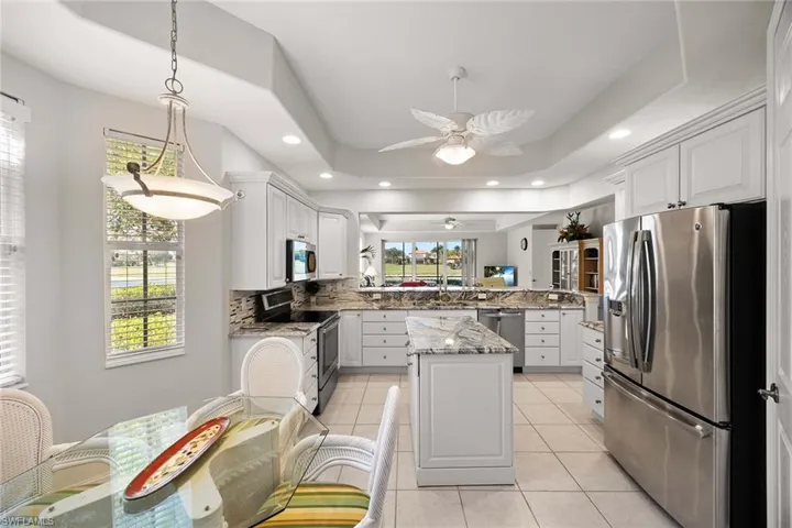 Kitchen with light stone countertops, stainless steel appliances, white cabinets, light tile patterned floors, and pendant lighting