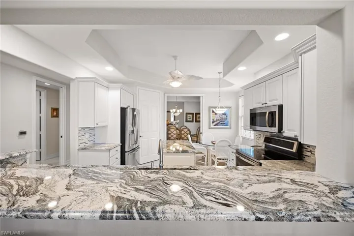 Kitchen with backsplash, decorative light fixtures, white cabinetry, appliances with stainless steel finishes, and light stone counters