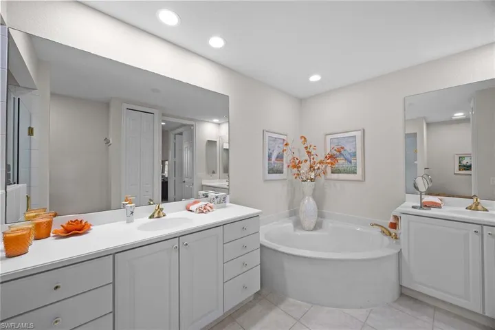 Bathroom with two vanities, a bath, light tile patterned flooring, recessed lighting, and a closet