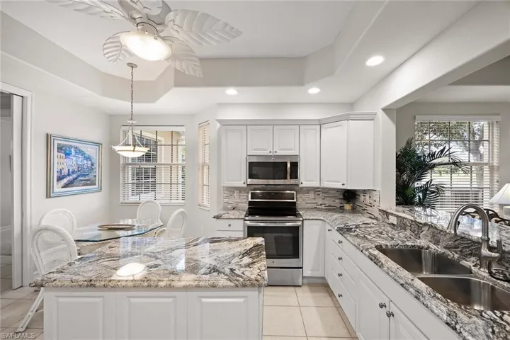 Kitchen featuring light stone counters, appliances with stainless steel finishes, decorative backsplash, white cabinetry, and light tile patterned floors