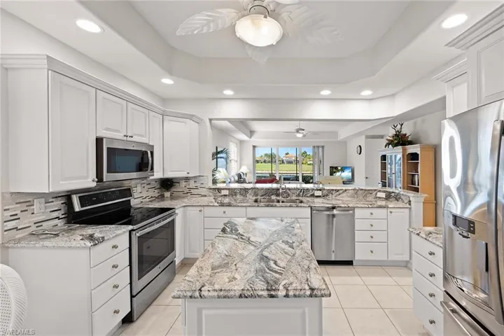 Kitchen with stainless steel appliances, a tray ceiling, white cabinets, light stone countertops, and a peninsula