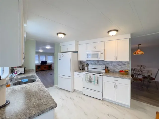 Kitchen with white appliances, white cabinets, decorative backsplash, and sink