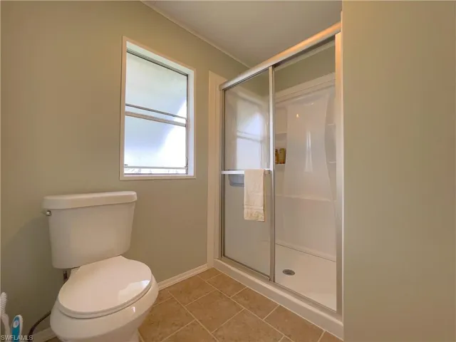Bathroom with toilet, a shower with door, and tile patterned floors